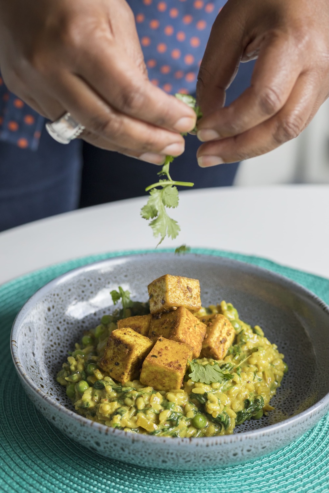Jax Hamilton garnishing a dish, hands sprinkling fresh coriander over a turmeric risotto