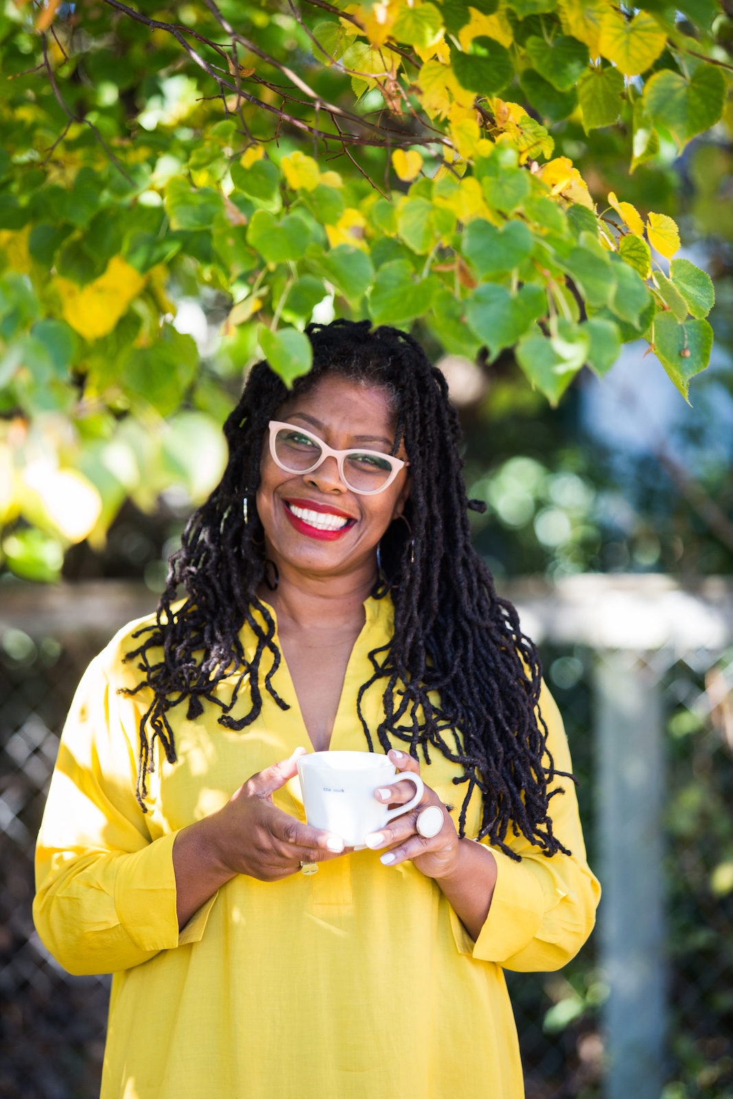Jax Hamilton outdoors in a yellow robe, smiling warmly with a cup of tea