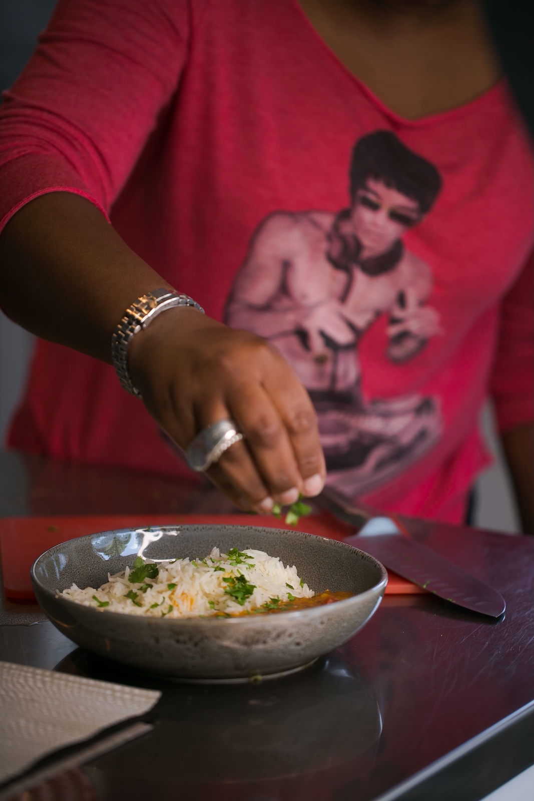 Jax Hamilton preparing a rice dish, hands adding fresh herbs at a cooking demonstration